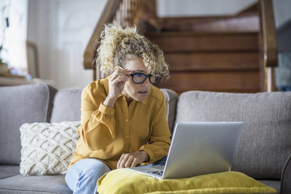 Surprised and worried adult woman reading bad notification on laptop computer at home in online
